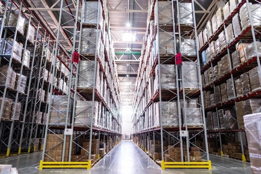 Corredor de galpão logístico com estruturas porta-palete altas e metálicas dos dois lados